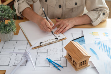 Engineer drawing blueprints for a sustainable house powered by a wind turbine, promoting renewable energy and ecological future