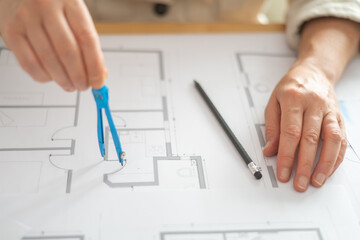 Architect using a compass to draw circles on a blueprint, with a pencil nearby, demonstrating the...