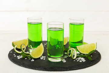 Sweet refreshing mint liqueur, with ice and mint leaves on table background, Shots with lime slice...