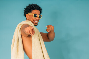 young latin man smiling with sunglasses and towel in swimsuit isolated on background, summer