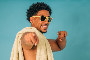 young latin man smiling with sunglasses and towel in swimsuit isolated on background, summer