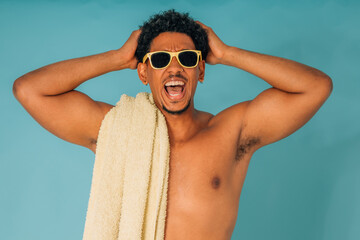young latino man shouting with sunglasses and towel in swimsuit isolated on background, summer