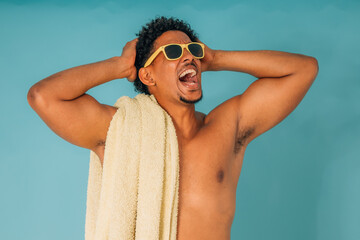 young latino man shouting with sunglasses and towel in swimsuit isolated on background, summer