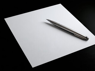 A silver pen rests on a blank white square paper atop a dark surface.  Subtle lighting casts a slight shadow