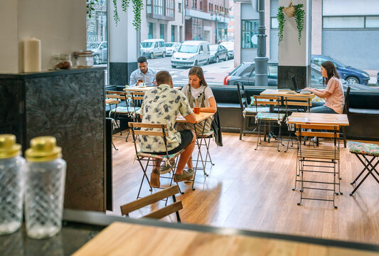 Customers enjoying coffee and working on laptops in a bright, inviting cafe, capturing the essence of modern cafe culture and urban lifestyle in a lively and social atmosphere
