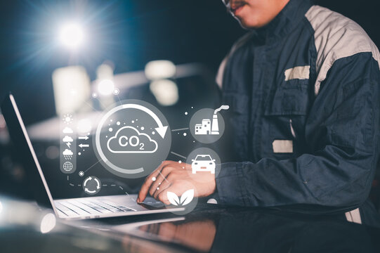 A person works on a laptop analyzing carbon dioxide emissions and environmental impact with futuristic digital icons displayed.