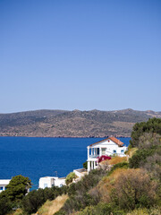 White Mediterranean house on a coastal hill on Milos Island, with sea and distant mountains under a cloudless sky.