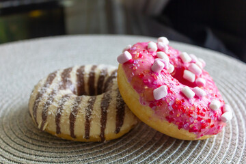 two donuts on kitchen table, pink donut with marshmallow and chocolate donut zebra, empty space for...