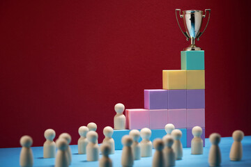 small trophy on top of toy block surround by wood figurines against red background