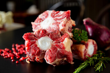 Fresh beef oxtails neatly arranged on a kitchen counter with herbs and spices. Flat lay showing raw...