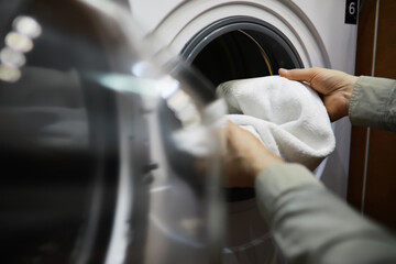 Hands Loading White Towel into Modern Washing Machine for Laundry at Home