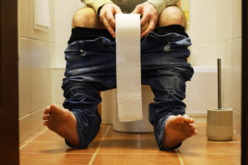 Man Sitting on Toilet with Rolled Toilet Paper in a Bathroom - Everyday Life, Hygiene, and Personal...