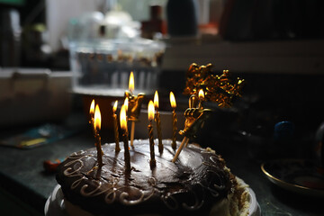 Chocolate Birthday Cake with Lit Candles in a Dark Kitchen Setting
