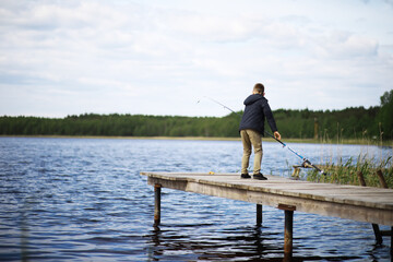 Fototapeta premium Boy Fishing on Wooden Dock by Lake in Peaceful Nature Setting