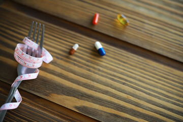 Measuring Tape Wrapped Fork with Pills on Wooden Table - Diet, Health, and Nutrition Concept