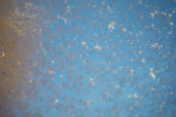 Close-Up of Frosty Frozen Snowflakes on Glass Pane with Clear Blue Sky Background