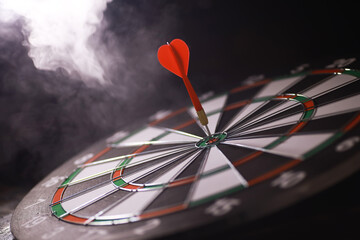 Bullseye Dartboard with Red Dart in Smokey Background - Precision Success Concept