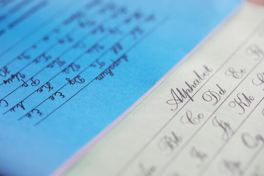 Close-up of Cursive Handwriting Practice Sheets with Calligraphy Alphabets and Blue Writing Paper