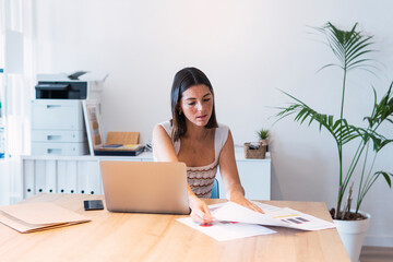 Businesswoman examining charts sitting with laptop at office
