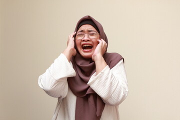 An Asian Muslim woman raising both of her hands, crying and screaming desperately.