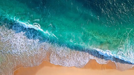 Aerial wave crashing against golden beach, green and white foam. 