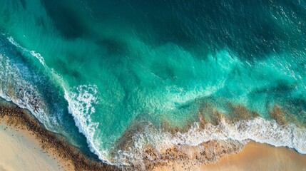 Aerial wave crashing against golden beach, green and white foam. 