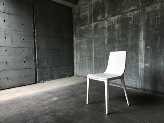 Minimalist Chair in Concrete Space: A modern, minimalist white chair stands alone in a stark concrete room, embodying simplicity and a sense of solitude in its architectural setting.