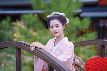 Traditional Japanese Woman in Furisode Kimono with red wagasa umbrella, fan, in a peaceful natural...