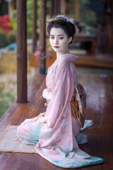 A pretty young Asian Japanese woman in a Traditional Yukata Dress. A Young Asian girl is wearing a beautiful pink kimono or  Furisode dress, sitting in front of the house.