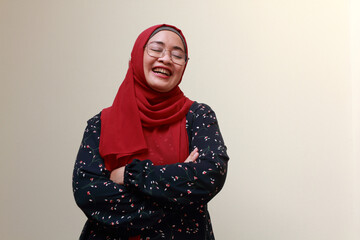 An Asian Muslim lady standing with her arms crossed and laughing. Happy and satisfied expression.