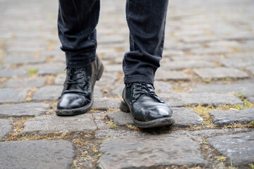 Black leather boots walking on cobblestone pavement in an urban setting during daylight hours