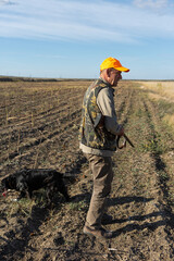 Mature man hunter with gun while walking on field.