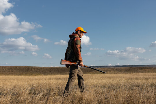 Mature man hunter with gun while walking on field.