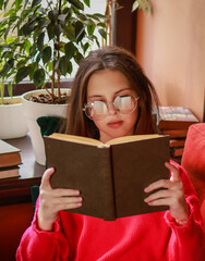 The girl is reading a book while sitting on the sofa.