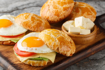 Delicious breakfast sandwiches with fried egg, butter, tomatoes, cheese, lettuce close-up on wooden board on table. horizontal