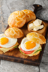 Bolo bao bun sandwich with fried egg, butter, tomato, cheese, lettuce close-up on wooden board on table. Vertical