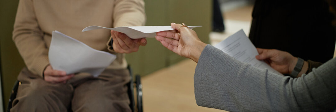 Header of man with disability handing document to woman during business meeting, both holding papers, focus on hands exchanging paperwork - Powered by Adobe