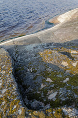 Moss-covered rock surface slopes gently into a calm lake, with visible cracks and algae at the waterline under soft light.