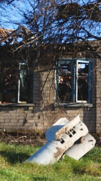 A shell from a multiple rocket launcher system sticks out of the ground against the background of a destroyed house. The Russian army is shelling Ukrainian villages. Russian-Ukrainian War 2022