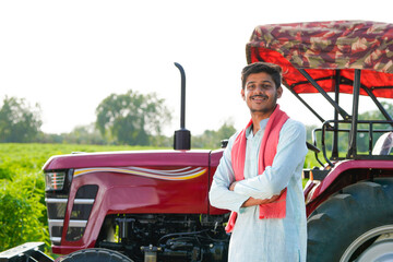 young indian farmer standing with tractor at field