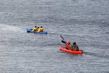 Two tandem kayaks with people in life jackets paddle across a calm lake, enjoying outdoor adventure...