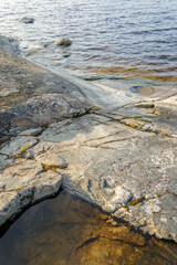 Close view of textured rocky shoreline and calm lake water with subtle ripples under soft evening light in nature.