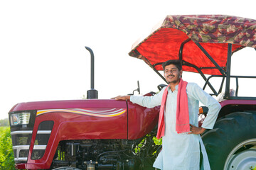 young indian farmer standing with tractor at field