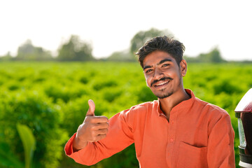 young indian farmer standing at green agricultural field