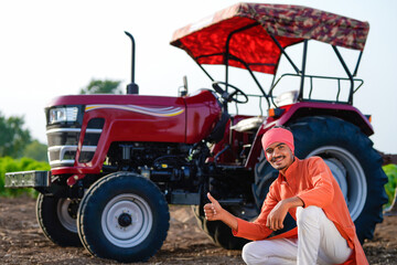 young indian farmer sitting with tractor at field