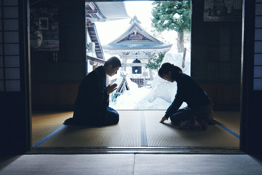 雪の日本寺院で互いに礼を交わす僧侶と女性