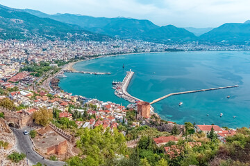 Aerial view of Alanya harbor and Red Tower with the vibrant city nestled between mountains and the Mediterranean Sea, Turkey. Serene turquoise waters surround this historic coastal town