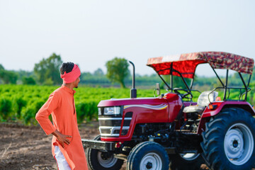 young indian farmer standing with tractor at field