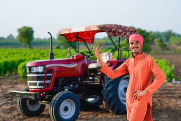 young indian farmer standing with tractor at field