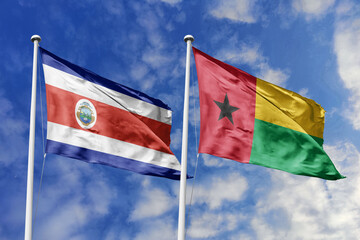 3D illustration. Costa Rica and Guinea-Bissau flags waving in the sky. High detailed waving flag. 3D render. Flags fluttered in the cloudy sky, symbolizing diplomatic relations.